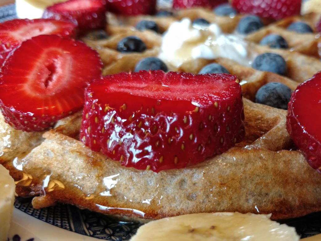 vegan sourdough waffles, closest side view, with strawberries, blueberries, coconut cream, and maple syrup