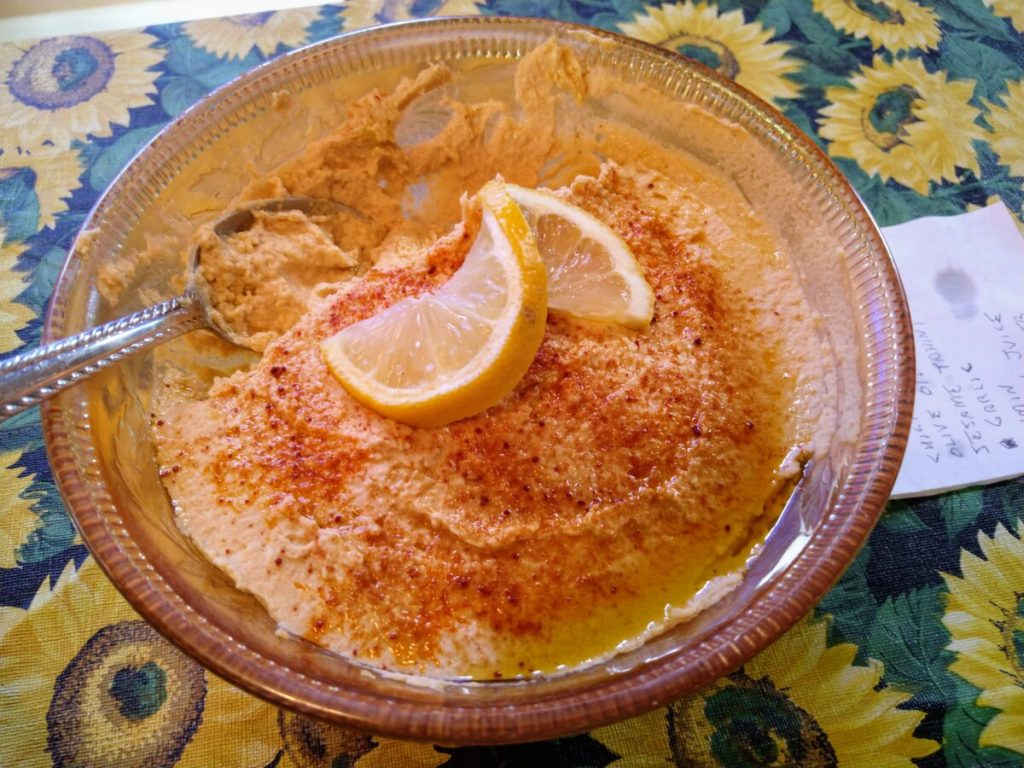 bowl of homemade vegan hummus, topped with fresh lemon and paprika, and drizzled with olive oil
